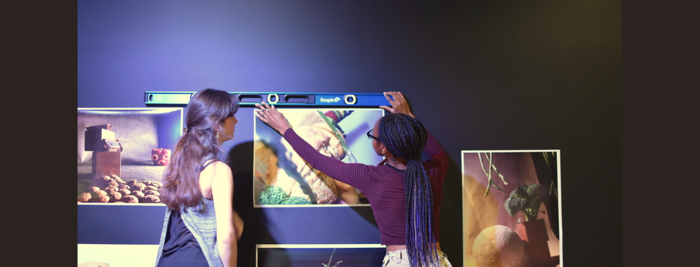 Two college students hanging up artwork in a gallery. One student is holding a level. 