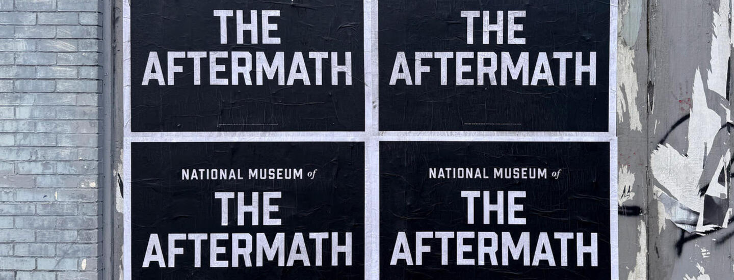 A wall with posters on it. The posters are black and white and read National Museum of the Aftermath 