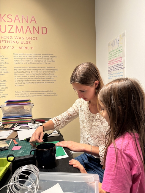 Two people are creating an art project together in a gallery space. One is older and one is younger. 