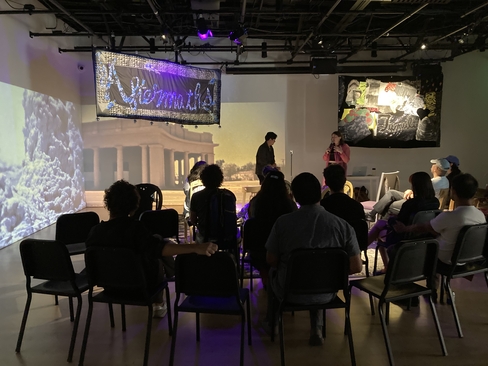 group photo of people sitting in Cauleen Smith's installation with two people speaking on a mic 