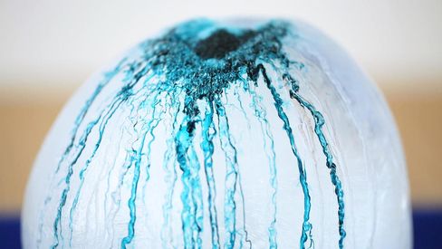 Frozen balloon of water with pigment dripping on the top 