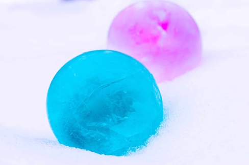 Two colorful frozen balls of water - one is pink and one is blue