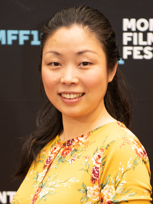 Nanfu Wang smiling in a yellow floral dress against a black background.