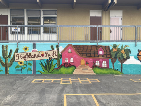 Colorful photograph of a wall with a mural painted on it depicting a pink house and a sign that says "Highland Park"