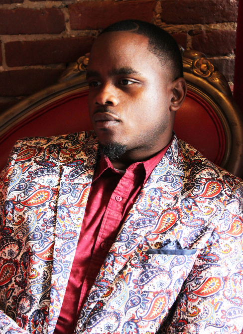 Portrait of Jonah Mixon-Webster, he is wearing a floral print suit and a pink shirt, looking into the distance.