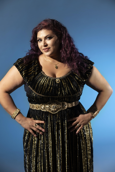 Esraa wearing a black dress with her hands on her hips against a blue background