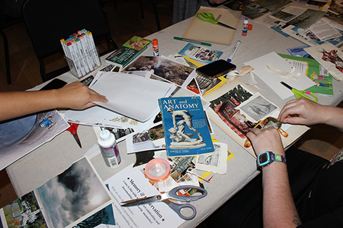 Magazines, scissors, glue and other materials on a table with hands creating a collage