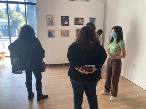 Photo of three people standing in an art gallery looking at paintings hung on the wall, their backs are turned away from the camera.