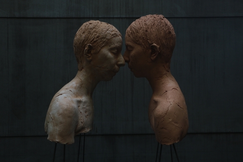 color image of two sculptural human busts in profile with faces touching