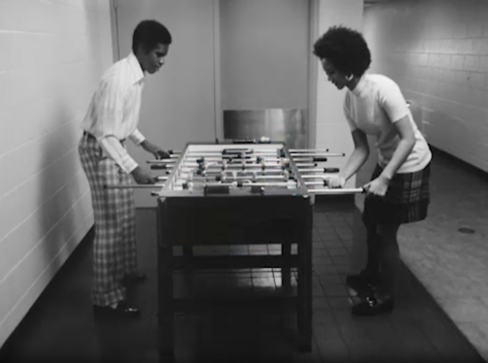 Black and white photograph of two Black people playing foosball 