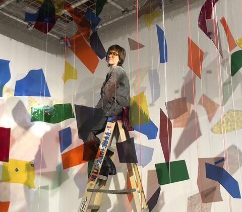Debra Scacco on a ladder in a colorful installation of rainbow pieces of glass