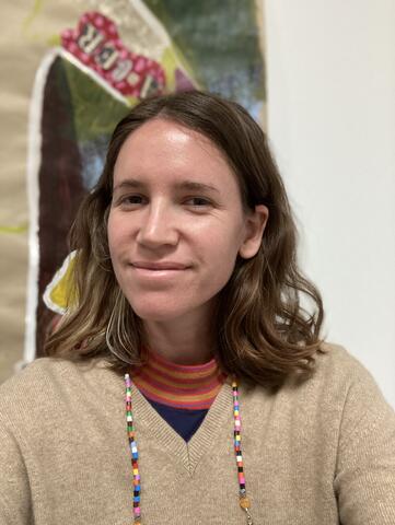 Portrait of Frankie Fleming. Frankie is smiling looking into the camera, standing in front of a colorful painting. 