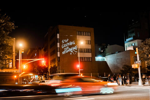 Nighttime city image with "stop gentrifying our neighborhoods" written on a building.
