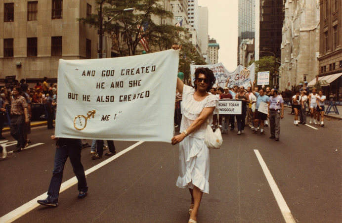Archival image of Sylvia Rivera walking in a protest holding a large banner 